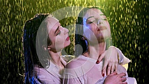 Young woman tenderly embraces lady while stands under rain