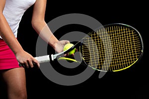 Young woman on a tennis practice. Beginner player holding a racket, learning basic skills. Portrait on black background.