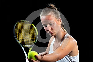 Young woman on a tennis practice. Beginner player holding a racket, learning basic skills. Portrait on black background.