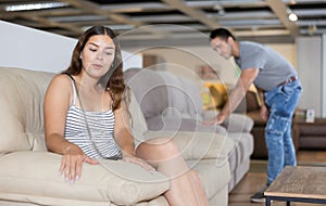 Young woman testing softness of sofa in furniture salon