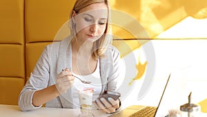 Young woman texting on smartphone and eating dessert in cafe