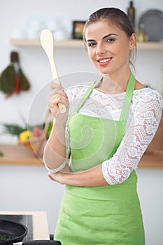 Young woman thinking about the menu while cooking in the kitchen. Housewife holding a wooden spoon in her hand