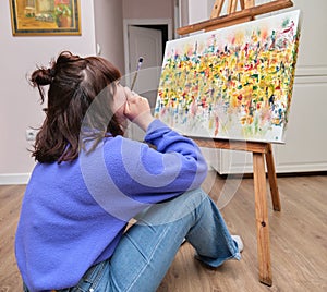 Young woman thinking and painting on canvas with oil paints at home