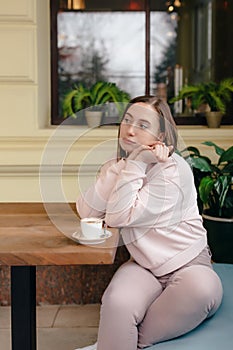 Young woman thoughtfully sits at the table with a cup of coffee