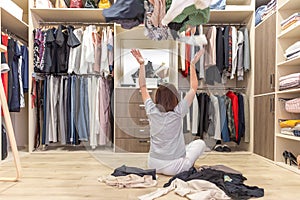 Young woman throwing clothes in walk in closet. Mess in wardrobe and dressing room photo