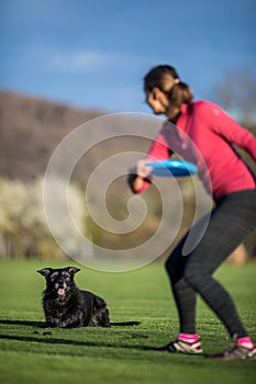 Young woman throwing freisbee to her black dog