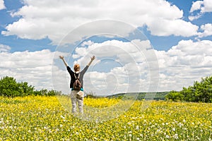 Young woman throwing up her ams standing on beautiful meadow full of yellow flowers