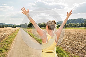 Young woman throwing up her ams at the start of rural road