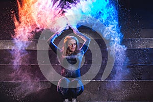 Young woman throws and dance with color powder on dark background