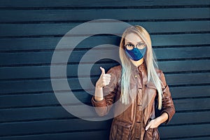 Young woman with thumbs up wearing protective face mask and eyeglasses