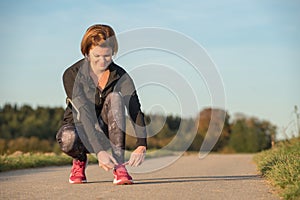 Young woman ties her running shoes outdoors