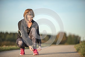 Young woman ties shoe laces of her jogging shoes