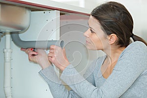 young woman tightening sink pipe with monkey wrench in kitchen
