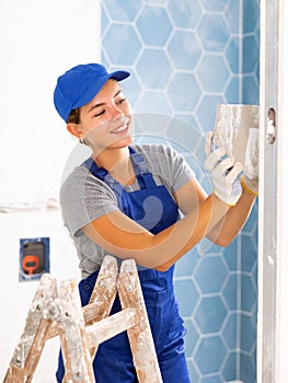 Young woman tiler glues ceramic tiles on the wall