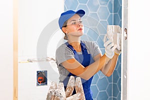 Young woman tiler glues ceramic tiles on the wall