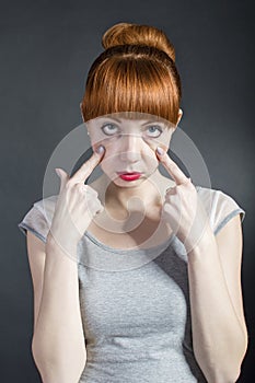 Young woman with tired eyes on black background. Negative facial