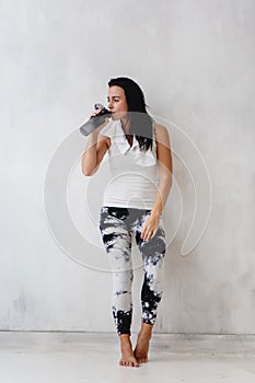Young woman tired after training drinking water leaning on the wall.