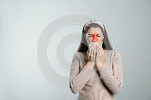 Young woman with tissue suffering from runny nose on light background. Space for text