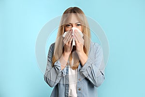 Young woman with tissue suffering from runny nose on light blue background