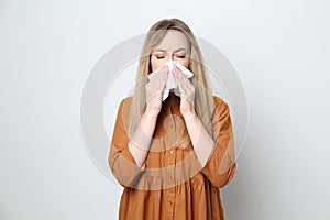 Young woman with tissue suffering from runny nose on white background