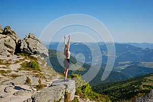 The young Woman at the top of the mountain raised her hands up on blue sky background. The woman climbed to the top and enjoyed