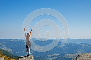 The young woman at the top of the mountain raised her hands up on blue sky background. The woman climbed to the top and enjoyed