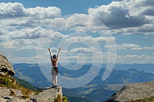 The young Woman at the top of the mountain raised her hands up on blue sky background. The woman climbed to the top and enjoyed