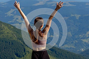 The young woman at the top of the mountain raised her hands up on blue sky background. The woman climbed to the top and enjoyed