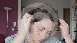 A young woman touches her short hair with her hands, showing her first gray hair. Early gray hair in women Life personal