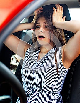 Young woman touching her head by hands while she sitting in a car.