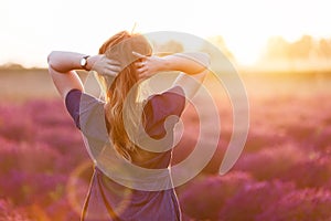 Young woman touching her long sombre hair looking at lavender field at sunset