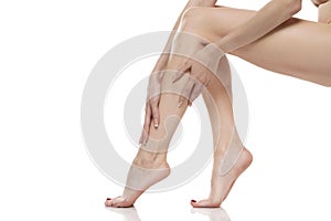 Young woman touching her smooth long legs, and putting on moisturizer after shaving her legs