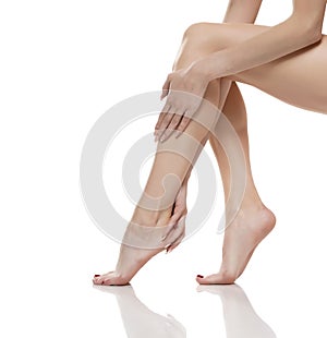 Young woman touching her smooth long legs, and putting on moisturizer after shaving her legs