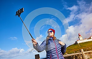 Young woman tourist at Cape Caba da Roca take a selfie shoots with view on beautiful landscape on a mobile phone, winter trip to photo