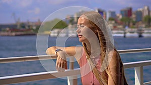 A young woman tourist enjoys a charming ferry boat ride in Istanbul, embracing the sea breeze as the city's skyline