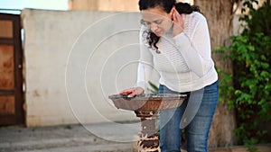 Young woman tourist, feeling thirst, drinking clean water flowing from a public water fountain