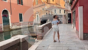 Young woman tourist got lost in venice and looks at the map on her mobile phone. A brunette woman admires the scenery of