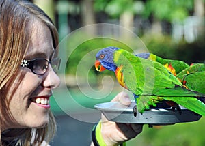 Young woman tourist happy smiling feeding Australian Rainbow Lorikeets birds