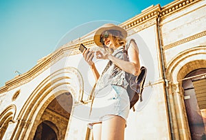Young woman tourist in hat with backpack using gps navigation on phone. Online booking. Summer fashion style. City tour. Explore t