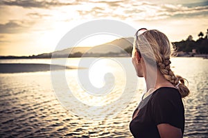 Young woman tourist looking into the sea horizon during beautiful sunset during summer beach holidays