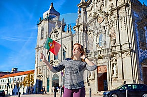 Young woman tourist with portuguese flag standing near the Congregados Carmelites church with famous portuguese blue tiles on the