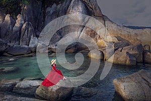 Young woman tourist in red dress sit on Hin Ta Hin Yai with blue sea and sky during summer travel at Koh Samui island