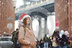 A young woman tourist in a Santa Claus hat walks during a snowfall in New York City on Christmas Eve. Manhattan Bridge and