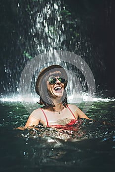 Young woman tourist smiling in the deep jungle with waterfall. Real adventure concept. Bali island.