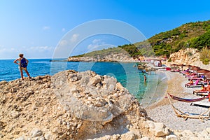 A young woman tourist standing on a rock and looking at beautiful beach in Proteas bay, Samos island, Greece