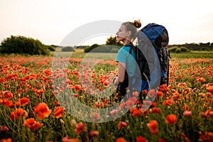 Young woman tourist stands on field of red poppies.
