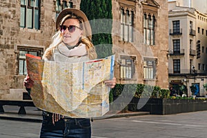 Young woman tourist stands on street of ancient European city and holds map. In background is beautiful building.
