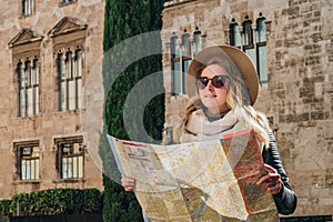 Young woman tourist stands on street of ancient European city and holds map. In background is beautiful building.