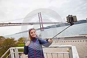 Young woman tourist take selfies on the background of famous iron 25th of April bridge in Lisbon city, Portugal