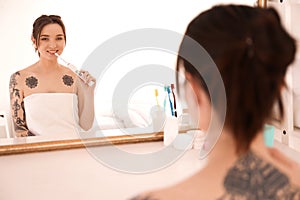 Young woman in towel brushing teeth near mirror at home. Morning routine